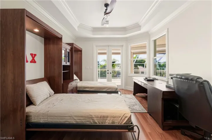 Bedroom featuring light wood-style floors, a raised ceiling, multiple windows, a desk, and crown molding