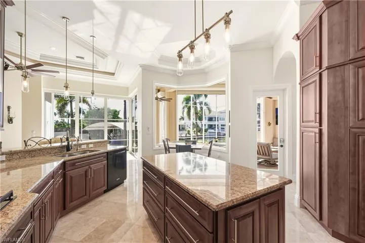 Kitchen with light stone countertops, pendant lighting, a kitchen island, black dishwasher, and ornamental molding