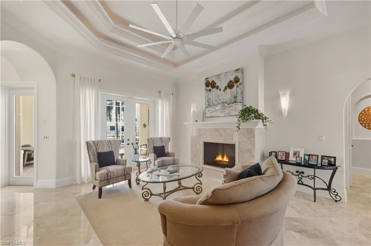 Living area featuring arched walkways, a raised ceiling, french doors, a premium fireplace, and ornamental molding