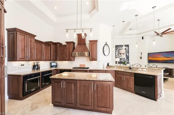 Kitchen featuring a raised ceiling, hanging light fixtures, a peninsula, a kitchen island, and black appliances