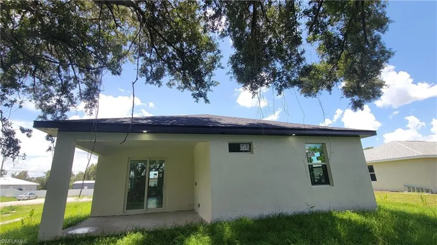 Rear exterior featuring a covered patio, sliding glass doors, white stucco finish, and a dark shingle roof