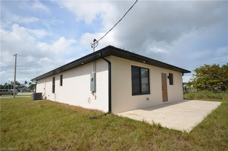 View of side of home with a yard, a patio, central AC unit, and stucco siding