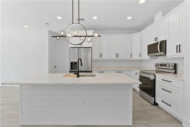 Kitchen with appliances with stainless steel finishes, light stone countertops, recessed lighting, hanging light fixtures, and a center island with sink