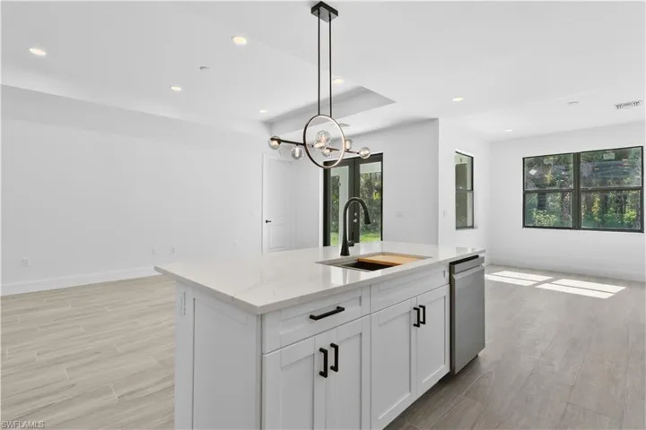 Kitchen with light stone counters, light wood finished floors, recessed lighting, hanging light fixtures, and white cabinets