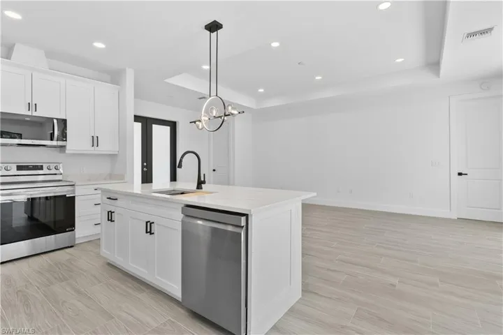 Kitchen featuring a raised ceiling, stainless steel appliances, white cabinetry, decorative light fixtures, and recessed lighting