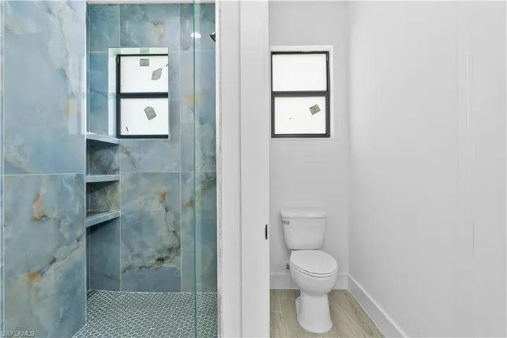 Bathroom with healthy amount of natural light and a marble finish shower