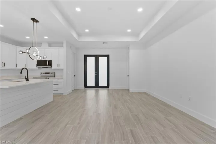 Kitchen with a raised ceiling, hanging light fixtures, white cabinetry, french doors, and wood tiled floors