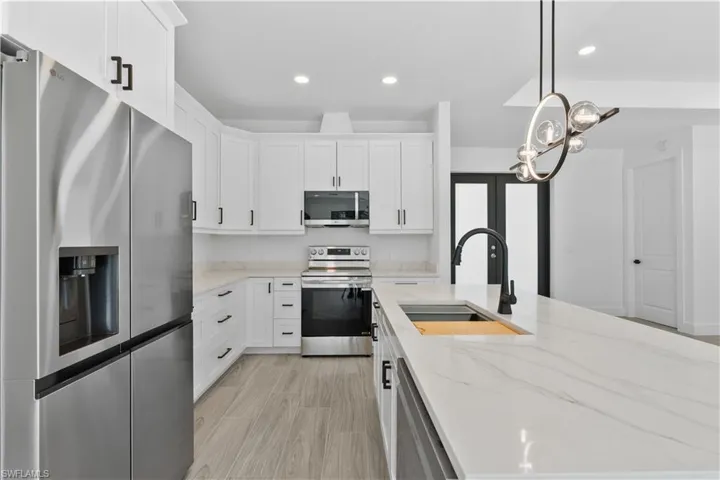 Kitchen featuring appliances with stainless steel finishes, light stone countertops, recessed lighting, pendant lighting, and white cabinetry