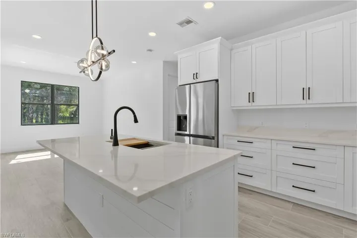 Kitchen featuring light stone countertops, white cabinets, recessed lighting, stainless steel fridge with ice dispenser, and a kitchen island with sink