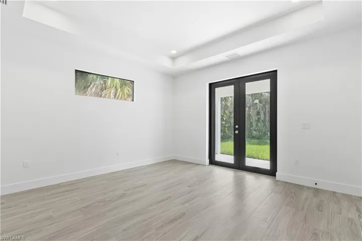 Spare room with light wood-style flooring, a tray ceiling, french doors, and recessed lighting