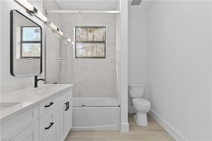 Full bathroom with bath / shower combo with glass door, double vanity, plenty of natural light, and light wood finished floors
