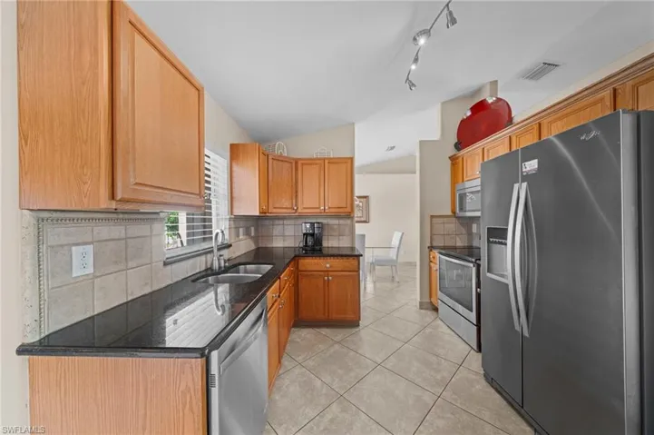 Kitchen featuring stainless steel appliances, dark stone countertops, lofted ceiling, tasteful backsplash, and light tile patterned flooring