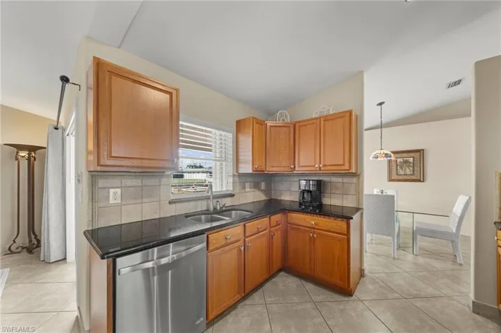 Kitchen featuring stainless steel dishwasher, lofted ceiling, tasteful backsplash, light tile patterned floors, and dark stone counters