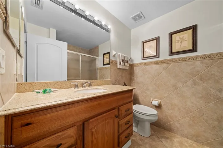 Full bathroom with vanity, light tile patterned floors, a stall shower, tile walls, and a wainscoted wall
