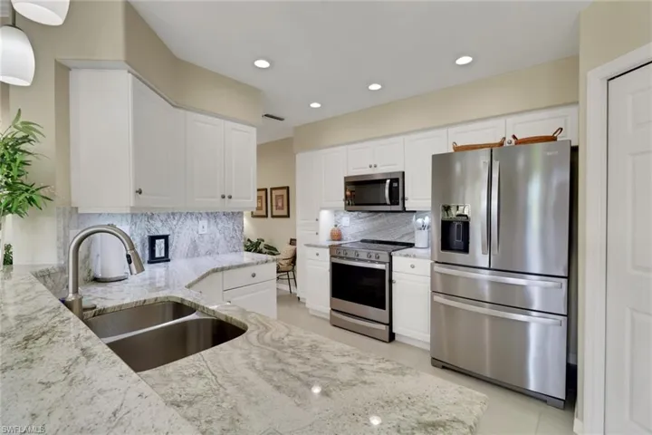 Kitchen with stainless steel appliances, light stone countertops, light tile patterned floors, white cabinets, and recessed lighting