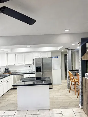 Kitchen with stainless steel fridge, dark countertops, dishwasher, and a center island