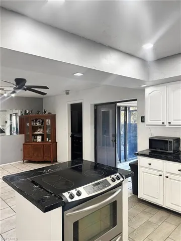 Kitchen featuring a kitchen island, stainless steel electric range, ceiling fan, white cabinets, and dark countertops