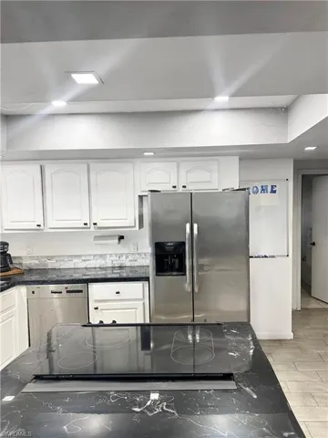 Kitchen with white cabinetry, stovetop, stainless steel fridge with ice dispenser, dishwashing machine, and wood tiled floor