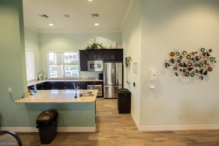 Kitchen featuring ornamental molding, appliances with stainless steel finishes, a peninsula, light wood-style flooring, and light stone countertops