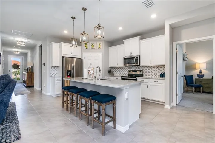 Kitchen featuring a breakfast bar area, decorative backsplash, appliances with stainless steel finishes, white cabinets, and pendant lighting