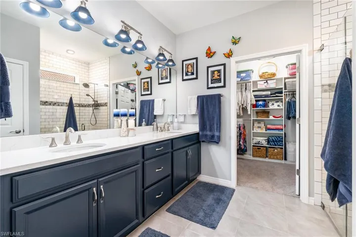 Full bathroom with light tile patterned flooring, a tile shower, double vanity, and a walk in closet