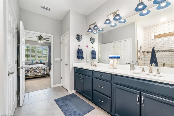 Ensuite bathroom with double vanity, light tile patterned flooring, a walk in shower, and ceiling fan