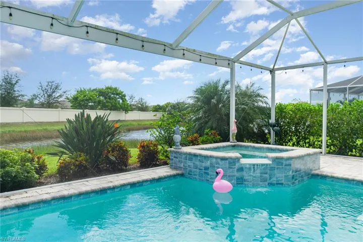 View of pool featuring glass enclosure, a pool with connected hot tub, a patio area, and a sunroom