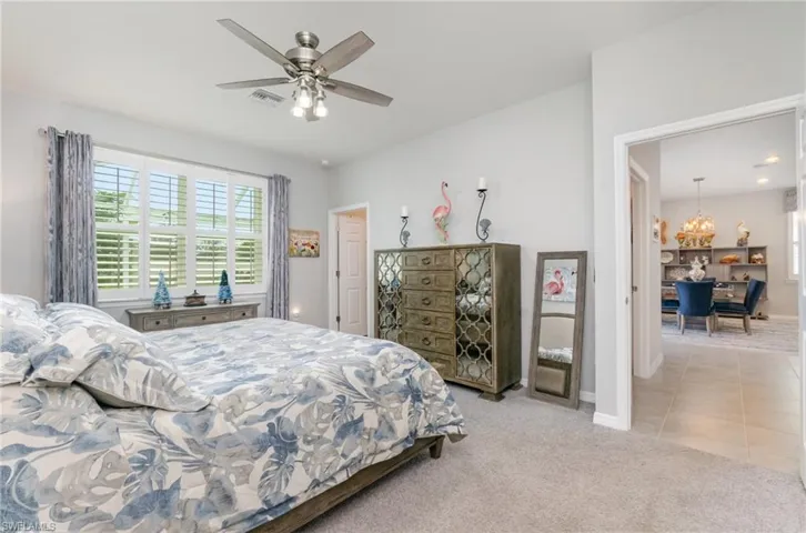 Bedroom featuring light colored carpet, a ceiling fan, light tile patterned floors, and a chandelier