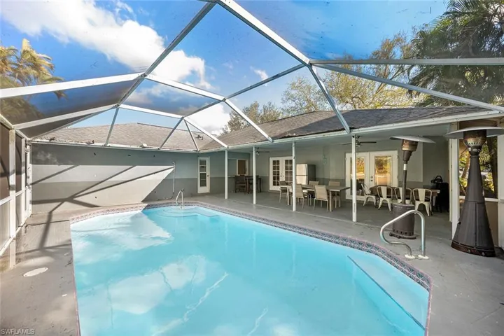 Outdoor pool featuring french doors, a sunroom, outdoor dining space, a patio, and glass enclosure