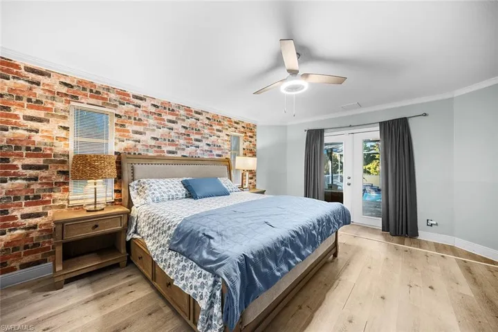 Bedroom featuring french doors, brick wall, light wood-style floors, access to exterior, and crown molding