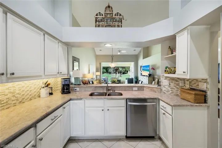Kitchen featuring dishwasher, white cabinetry, light stone countertops, decorative backsplash, and a high ceiling