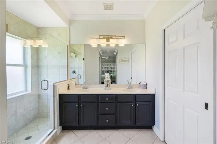 Bathroom featuring double vanity, a stall shower, crown molding, connected bathroom, and light tile patterned floors