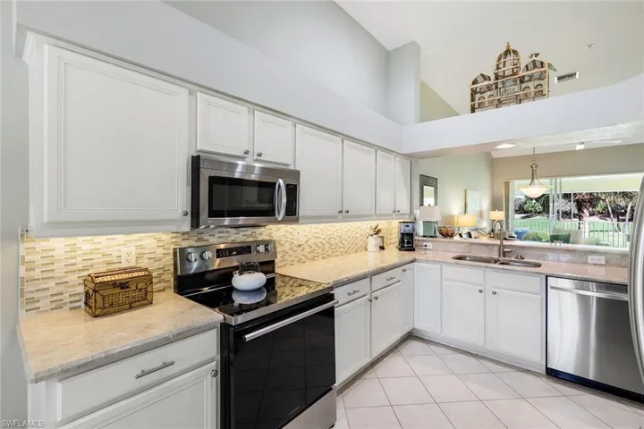 Kitchen with stainless steel appliances, white cabinetry, light stone counters, a high ceiling, and light tile patterned flooring