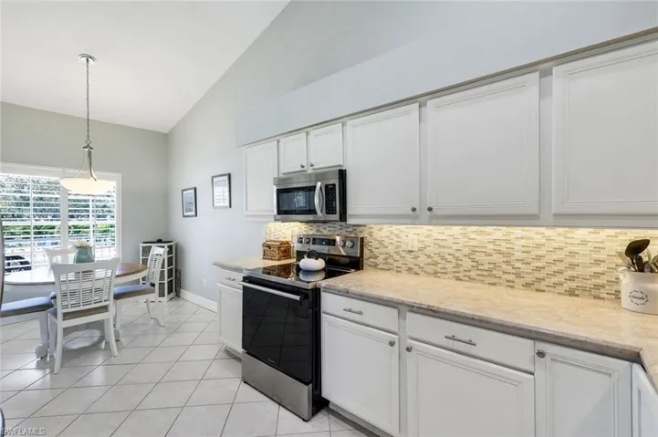 Kitchen featuring stainless steel appliances, backsplash, decorative light fixtures, white cabinets, and vaulted ceiling