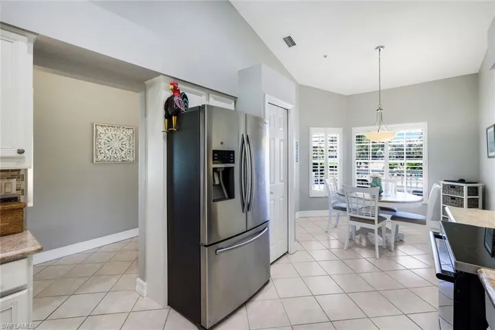 Kitchen with stainless steel fridge, white cabinetry, black range with electric cooktop, light tile patterned flooring, and vaulted ceiling