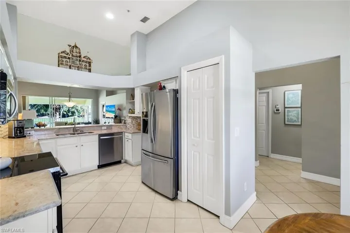 Kitchen with light tile patterned floors, stainless steel appliances, light stone countertops, a high ceiling, and white cabinetry