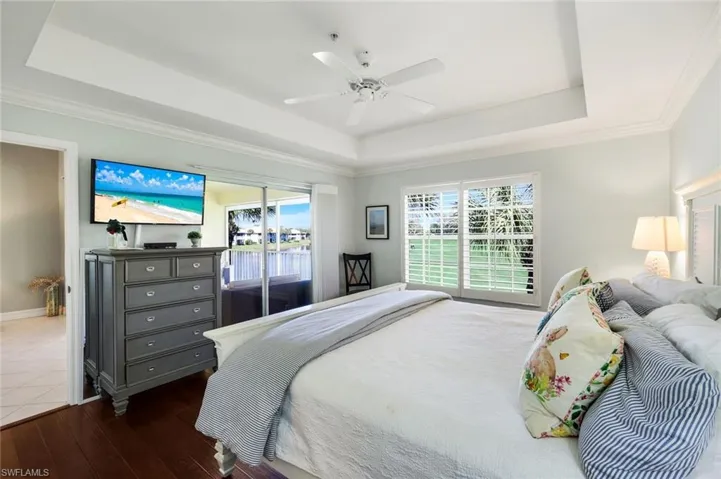 Bedroom featuring a raised ceiling, a ceiling fan, crown molding, multiple windows, and hardwood / wood-style flooring