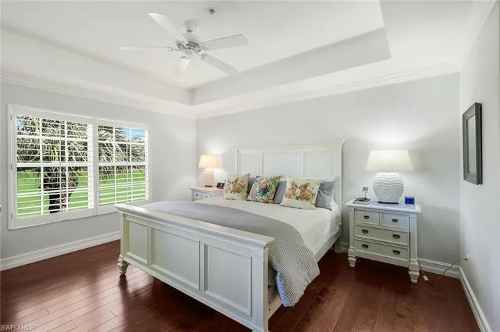 Bedroom featuring ornamental molding, dark wood-style flooring, a ceiling fan, and a tray ceiling