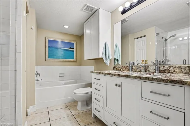 Bathroom featuring vanity, a textured ceiling, a stall shower, light tile patterned flooring, and a bath