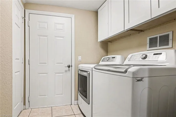 Laundry room with a textured wall, cabinet space, washer and dryer, and light tile patterned floors