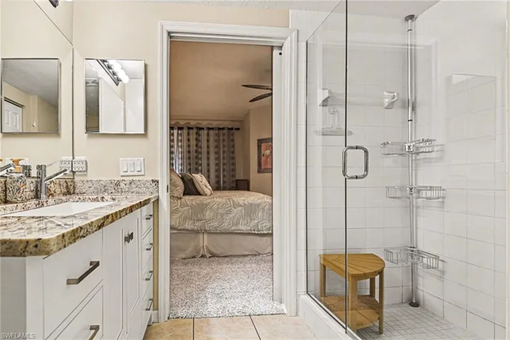 Ensuite bathroom with vanity, light tile patterned floors, a stall shower, ceiling fan, and light colored carpet