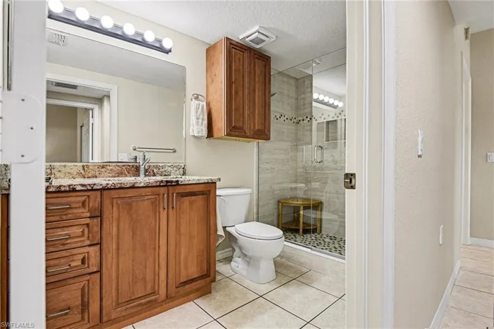 Full bath with vanity, a shower stall, a textured ceiling, and light tile patterned floors