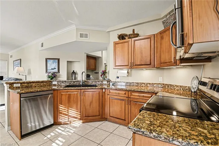 Kitchen with wood finish cabinets, a peninsula, ornamental molding, stainless steel appliances, and dark stone counters