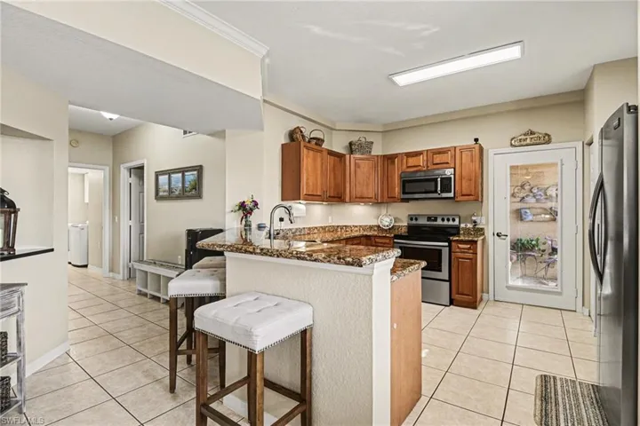Kitchen with stainless steel appliances, wood finish cabinetry, light tile patterned floors, a breakfast bar area, and ornamental molding