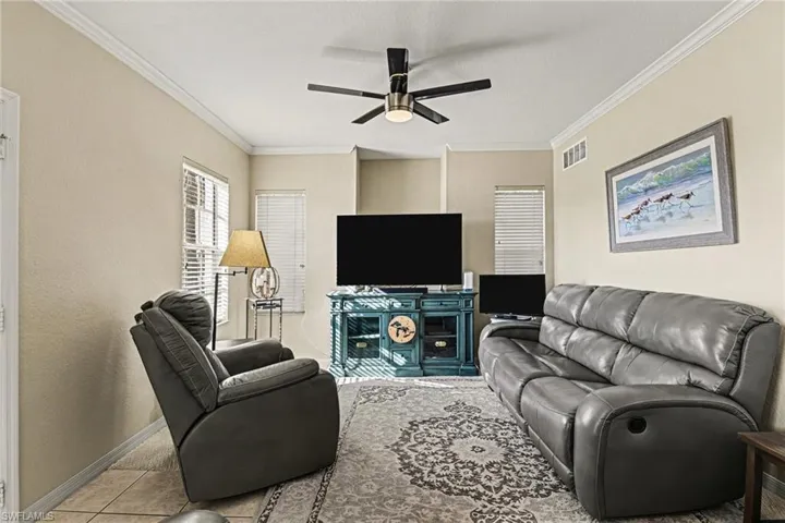 Living room featuring ceiling fan, crown molding, and light tile patterned floors