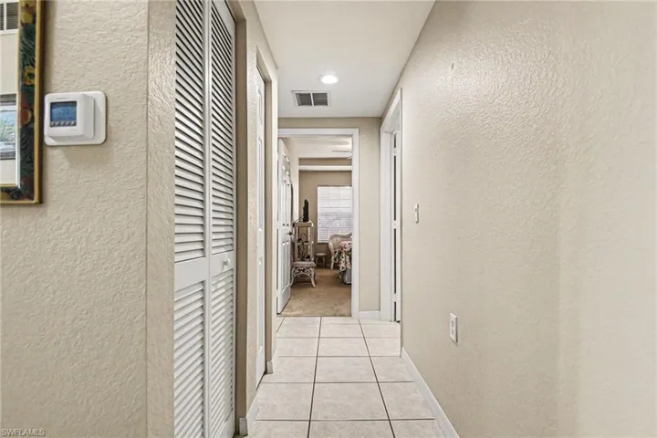 Hall featuring a textured wall, light tile patterned flooring, and recessed lighting