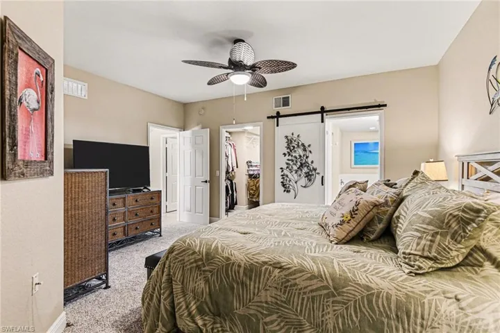 Bedroom featuring carpet, a barn door, ensuite bath, a spacious closet, and ceiling fan