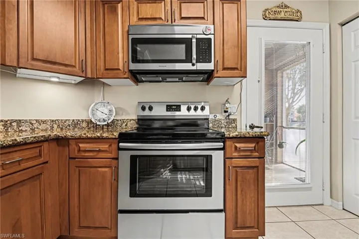 Kitchen with stainless steel appliances, wood finish cabinetry, dark stone countertops, and light tile patterned floors