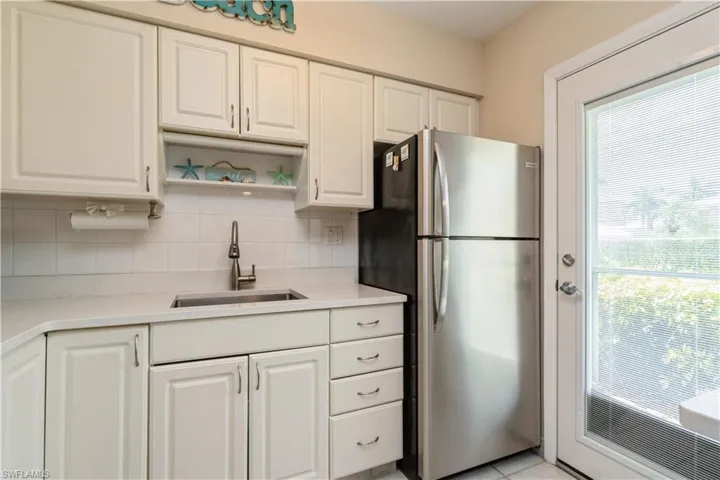 Kitchen featuring white cabinetry, decorative backsplash, stainless steel refrigerator, and sink