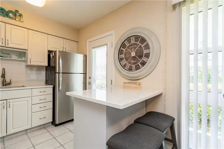 Kitchen with white cabinets, backsplash, sink, stainless steel fridge, and a kitchen breakfast bar